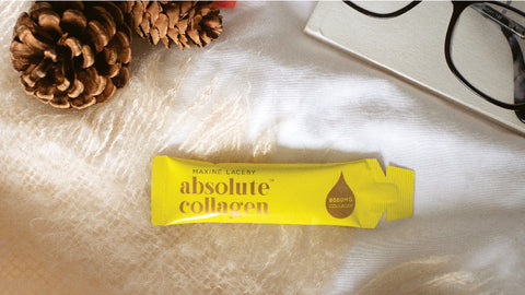 Photo showing a yellow sachet of Absolute Collagen laying on a soft white background alongside a pine cone to signify autumn weather
