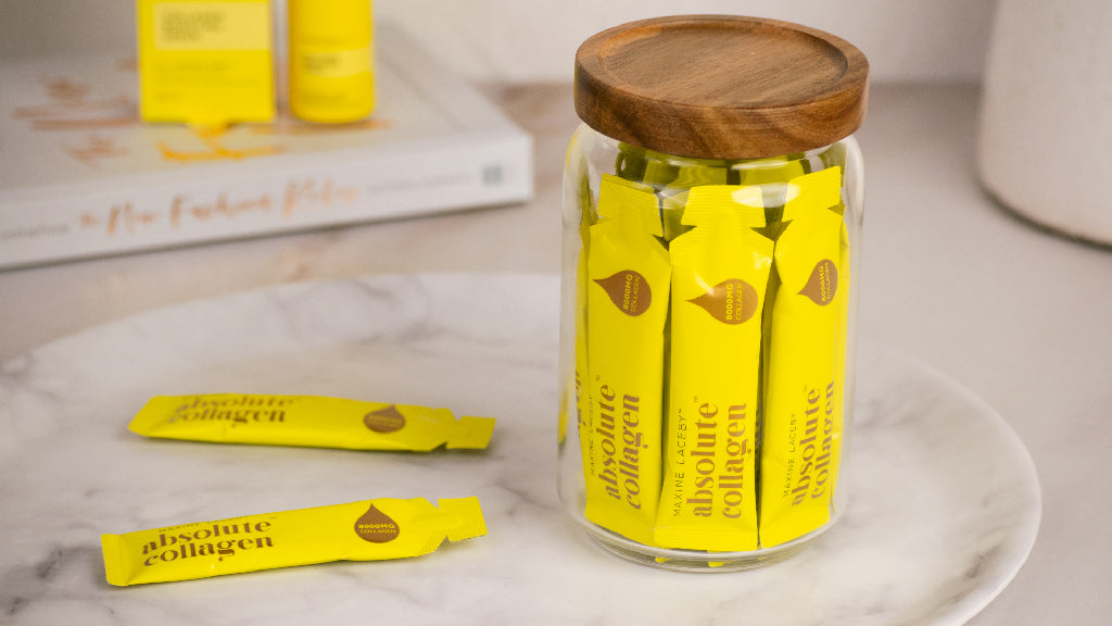 Photo showing a clear jar of yellow Absolute Collagen sachets with two Absolute Collagen sachets laying beside it on a beige ceramic plate