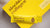 Close up photo showing a yellow sachet of Original Lemon Absolute Collagen laying atop a yellow Absolute Collagen box, with a grey surface visible in the background