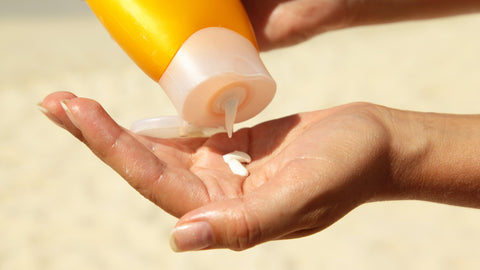 Photo showing some suncream being squeezed into a white person's hand on a beach