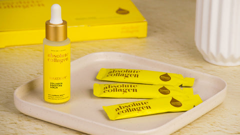 Photo showing three sachets of Absolute Collagen on a beige tray alongside a bottle of Maxerum. A box of Absolute Collagen stands in the background.