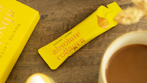 Photo showing a flatlay of a yellow Absolute Collagen sachet on a wooden table beside a cup of tea