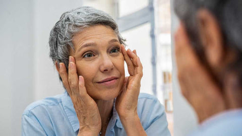 Photo showing a lady with short grey hair wearing a light blue top and looking in the mirror
