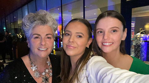 Photo showing Maxine Laceby and her two daughters at an awards entry. They are all white women smiling at the camera - Maxine has short grey hair and her daughters are in their twenties and have dark hair.