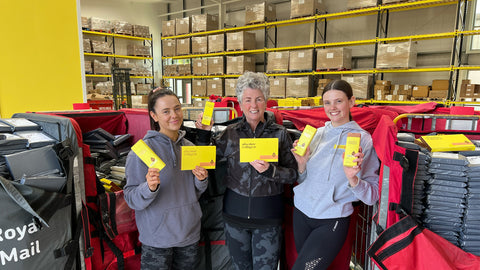 Photo showing Margot, Maxine, and Darcy Laceby wearing grey casual clothes and standing in the Absolute Collagen warehouse, they are holding boxes of Absolute Collagen and smiling