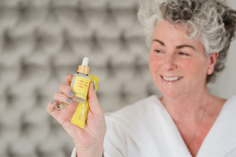 Maxine Laceby holding a yellow Absolute Collagen bottle and sachet and smiling against a grey background