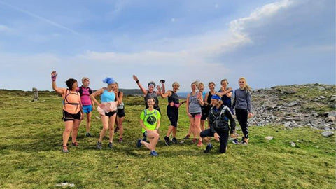 Photo showing a group of white women in running gear standing on a hill against a blue sky, with a white man crouching in front of them