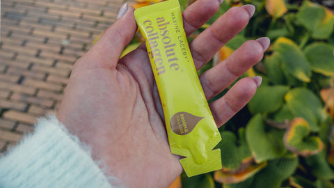 Photo of a white woman's outstretched hand holding a sachet of Absolute Collagen
