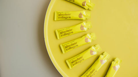 Photo showing a crescent of Absolute Collagen sachets lying flat on a yellow and grey background