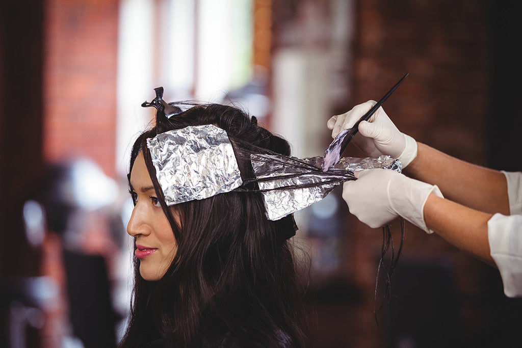 Photo of a brunette woman having silver foils applied by a hairdresser with gloved hands