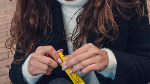 Photo of a woman with long wavy brown hair, she is holding a yellow Absolute Collagen sachet in her hands