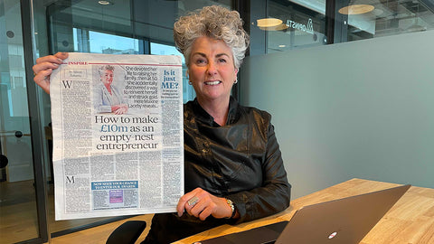 Photo showing Maxine Laceby smiling and holding up a copy of the Daily Mail containing an interview with her, she is smiling and sitting at a wooden desk in an office